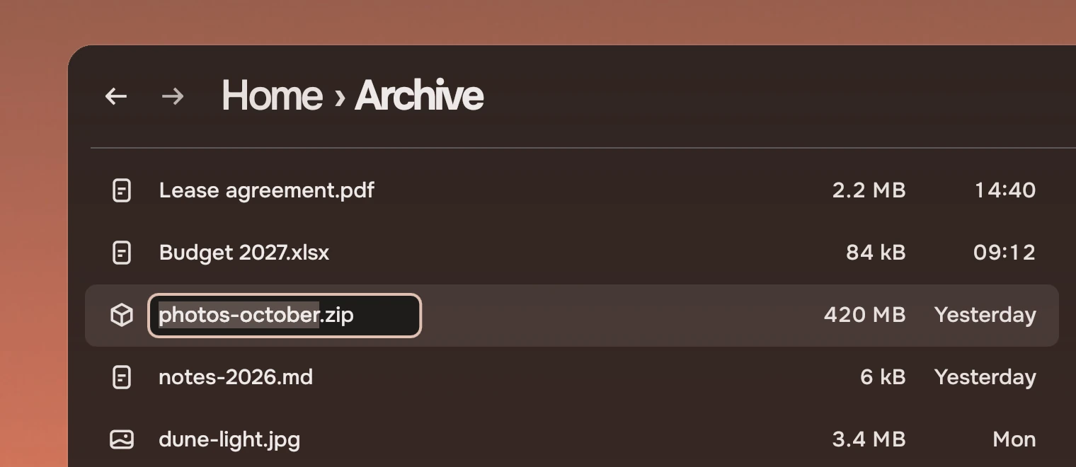 Part of a Files window headed Home, Archive, with a list of files. The name of the third, photos-october.zip, is being edited in its row: the name without its type is chosen, inside a box with an accent ring.